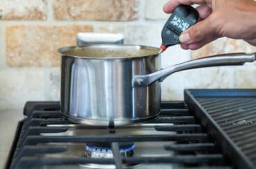 Someone temping caramel sauce in a silver saucepan.