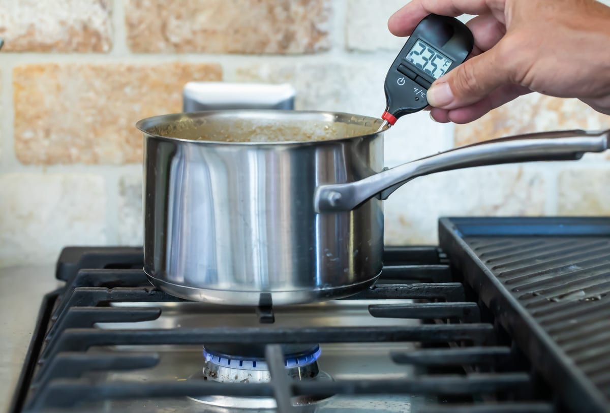 Someone temping caramel sauce in a silver saucepan.