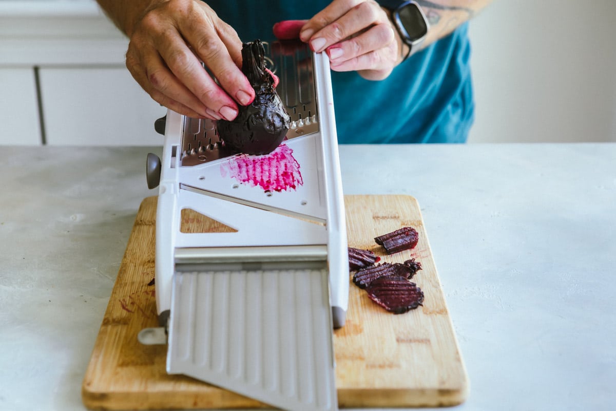 Beets being sliced on a mandoline slicer.