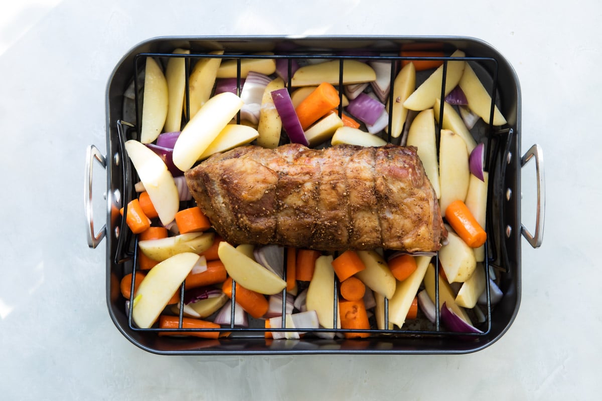 Pork on a roasting rack over vegetables before being cooked.