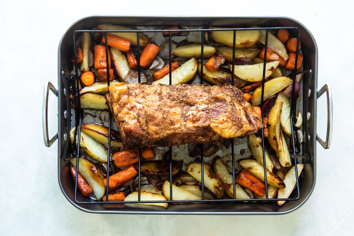 Roast pork on a roasting rack over vegetables.