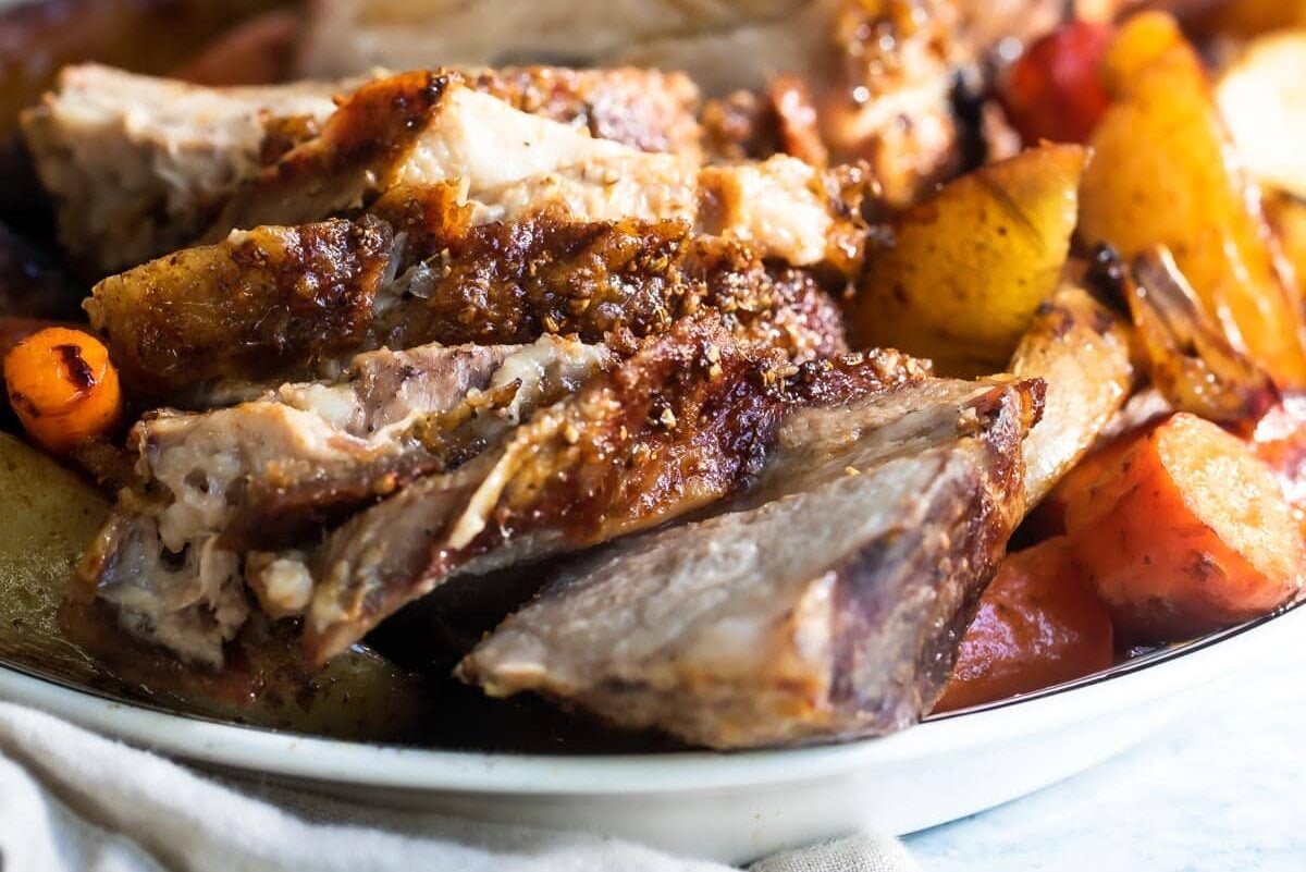 Slices of pork roast on a white plate next to vegetables.