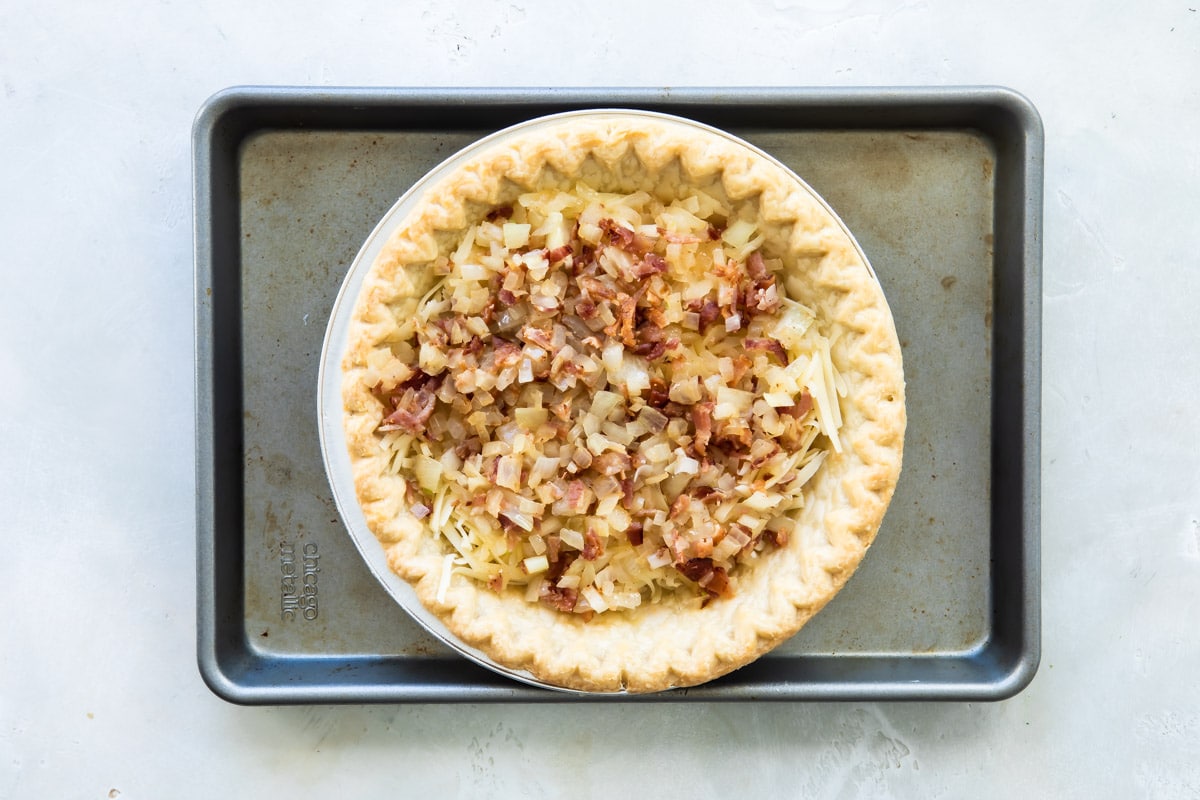 A quiche Lorraine in a pie tin before egg mixture has been added.