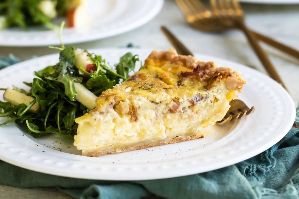 A slice of quiche Lorraine on a white plate.