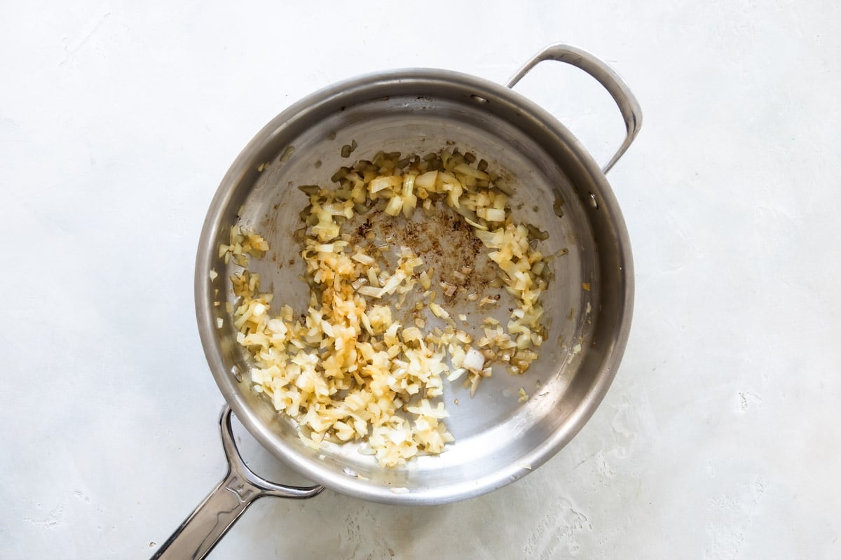 Onion being cooked in a silver skillet.