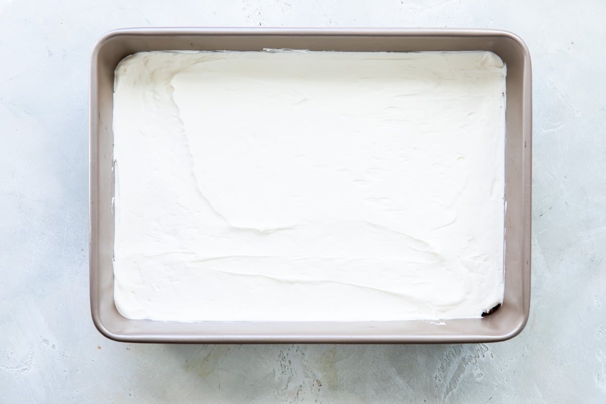 White cream on top of a pretzel crust in a baking pan.