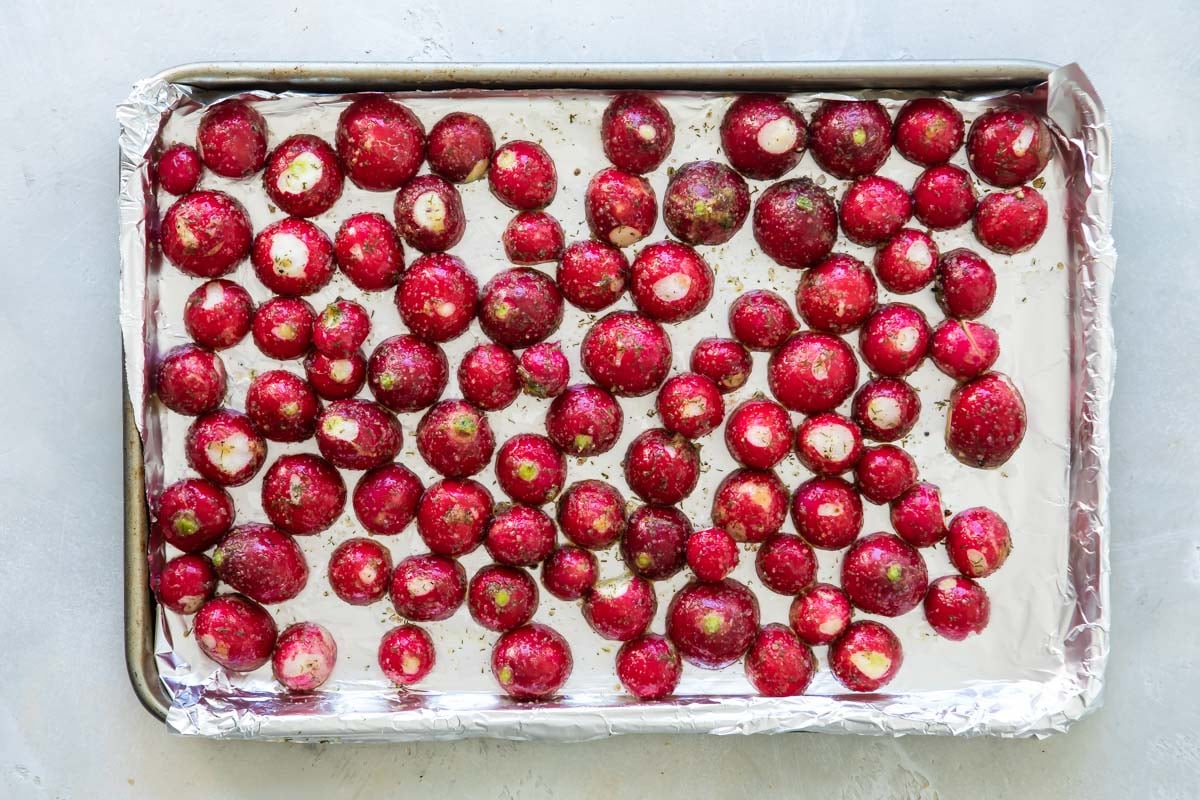 Seasoned raw radishes on a baking sheet.