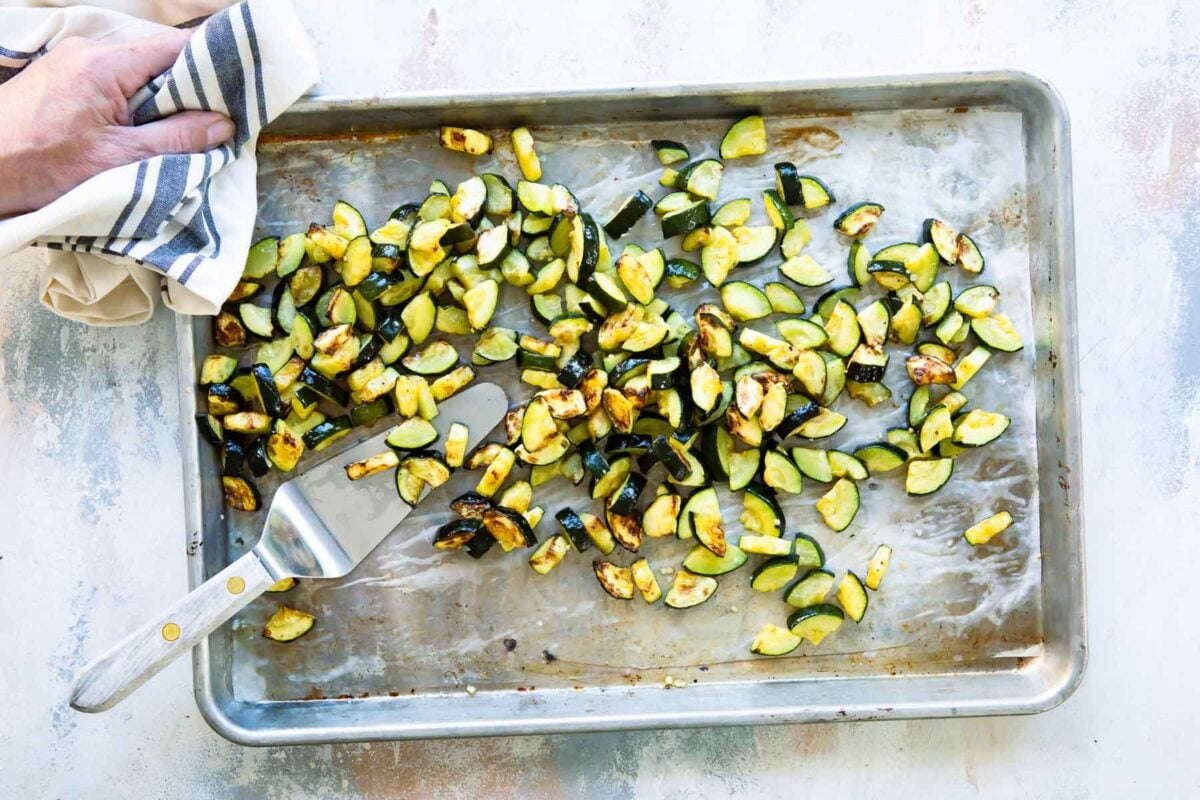 Roasted zucchini on a silver baking sheet.