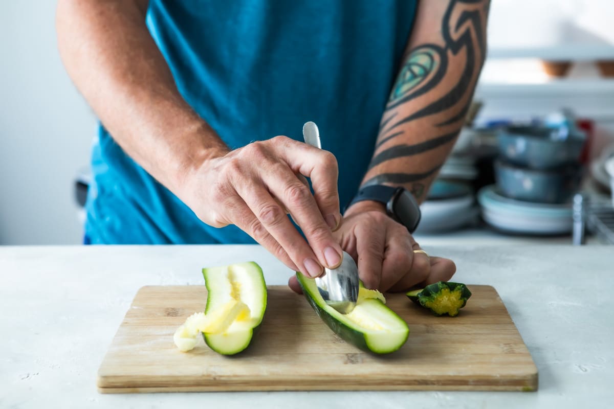 Someone scooping out the inside of a zucchini with a spoon.