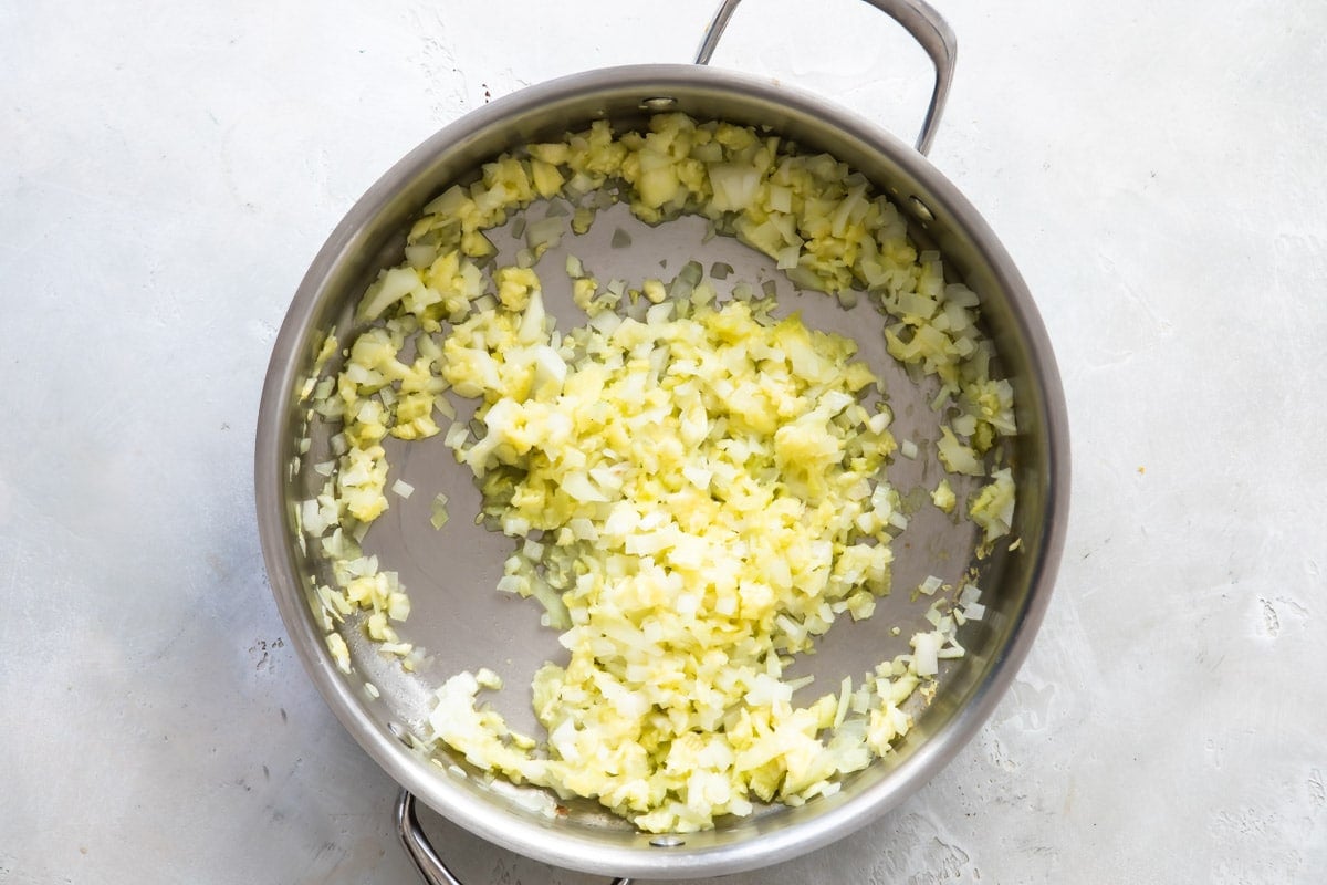 Onion being cooked in a silver skillet.