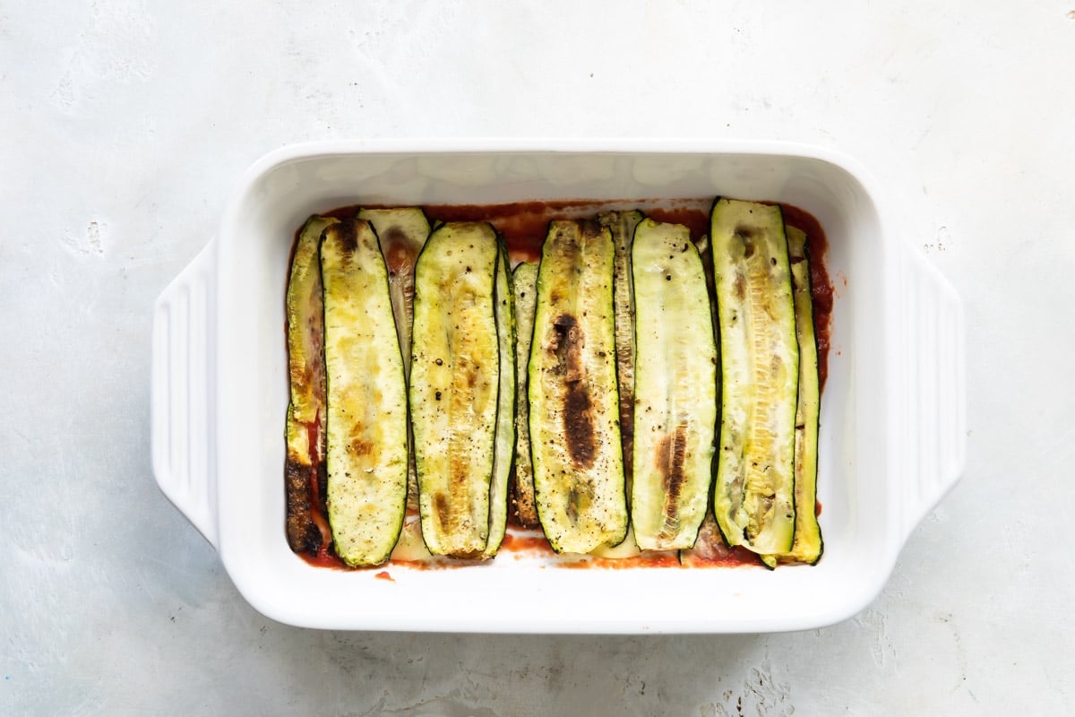 A partially assembled baking dish of Zucchini Parmesan before being baked.