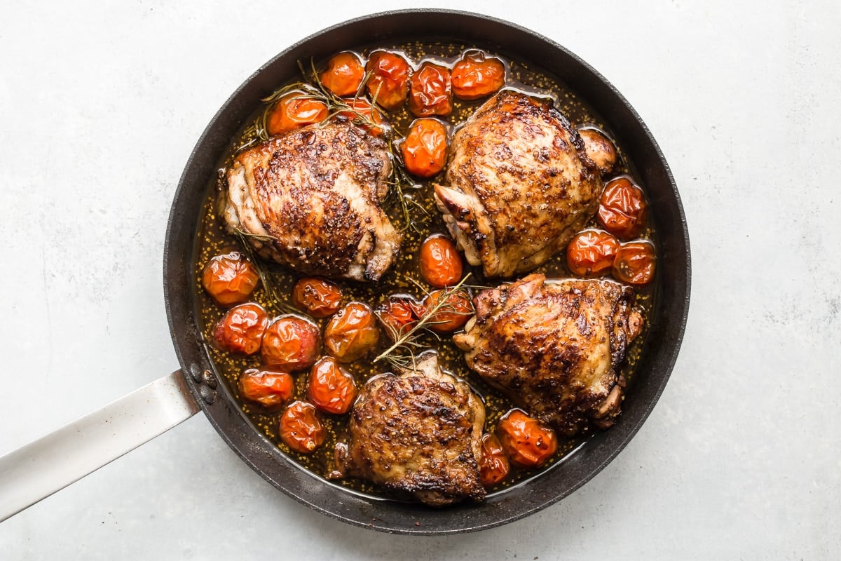 Cooked balsamic chicken and tomatoes in a black skillet.
