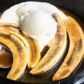 Bananas foster in a black skillet with a serving spoon resting in it.