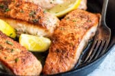 Salmon in a cast iron skillet with lemons for garnish.