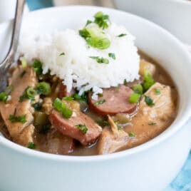 Chicken gumbo in a small white bowl with rice on top.