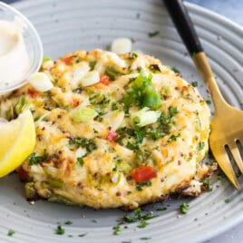 A crab cake on gray plate with a lemon wedge garnish.
