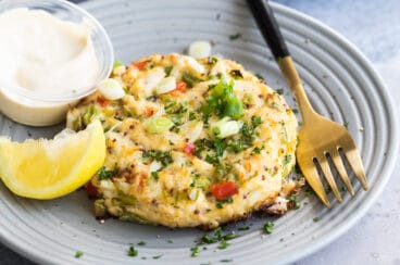 A crab cake on gray plate with a lemon wedge garnish.