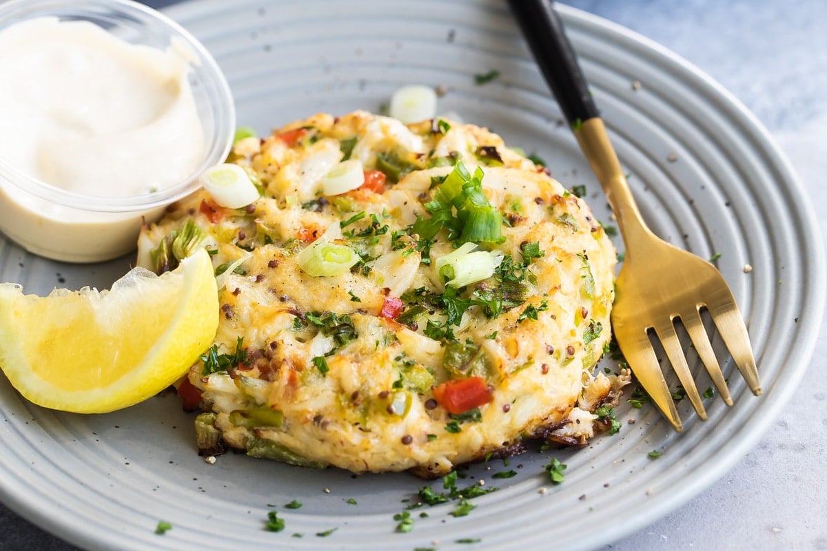 A crab cake on gray plate with a lemon wedge garnish.
