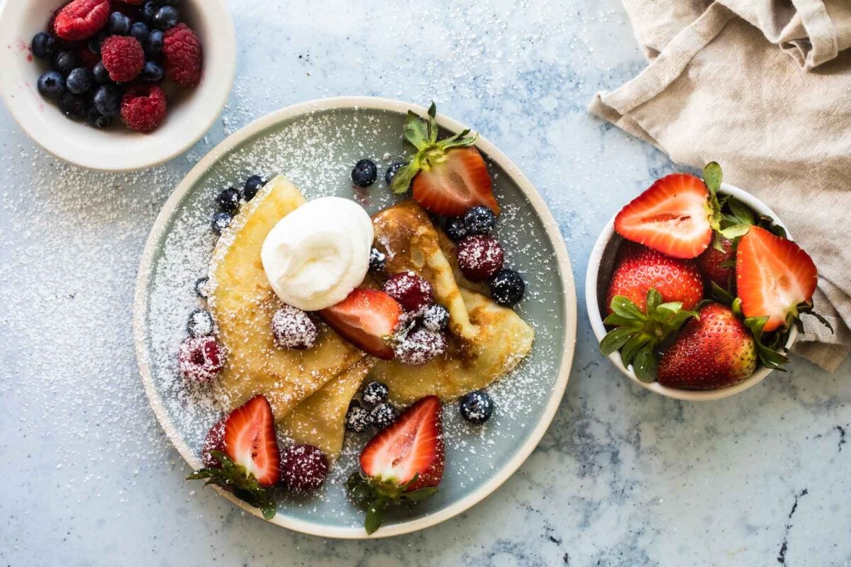A plate of crepes with whipped cream and berries on top.