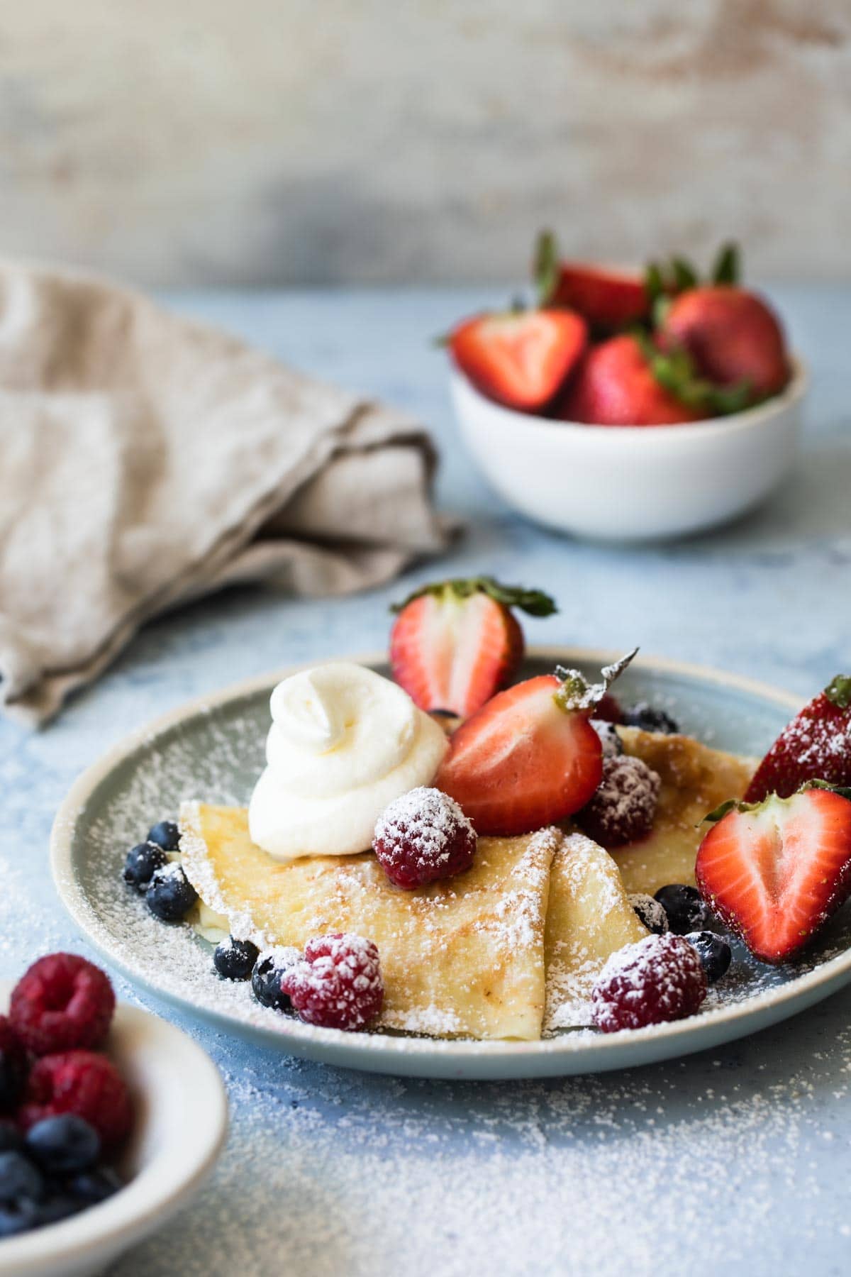 A plate of crepes with whipped cream and berries on top.