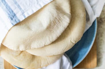 Three pieces of homemade pita bread wrapped in a linen towel on a blue plate.