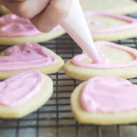 Someone frosting heart sugar cookies with pink royal icing.