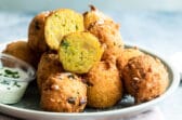 Hush puppies on a light blue plate with white dipping sauce.
