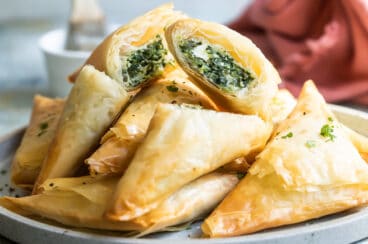 A pile of three cheese spanakopita triangles on a plate.