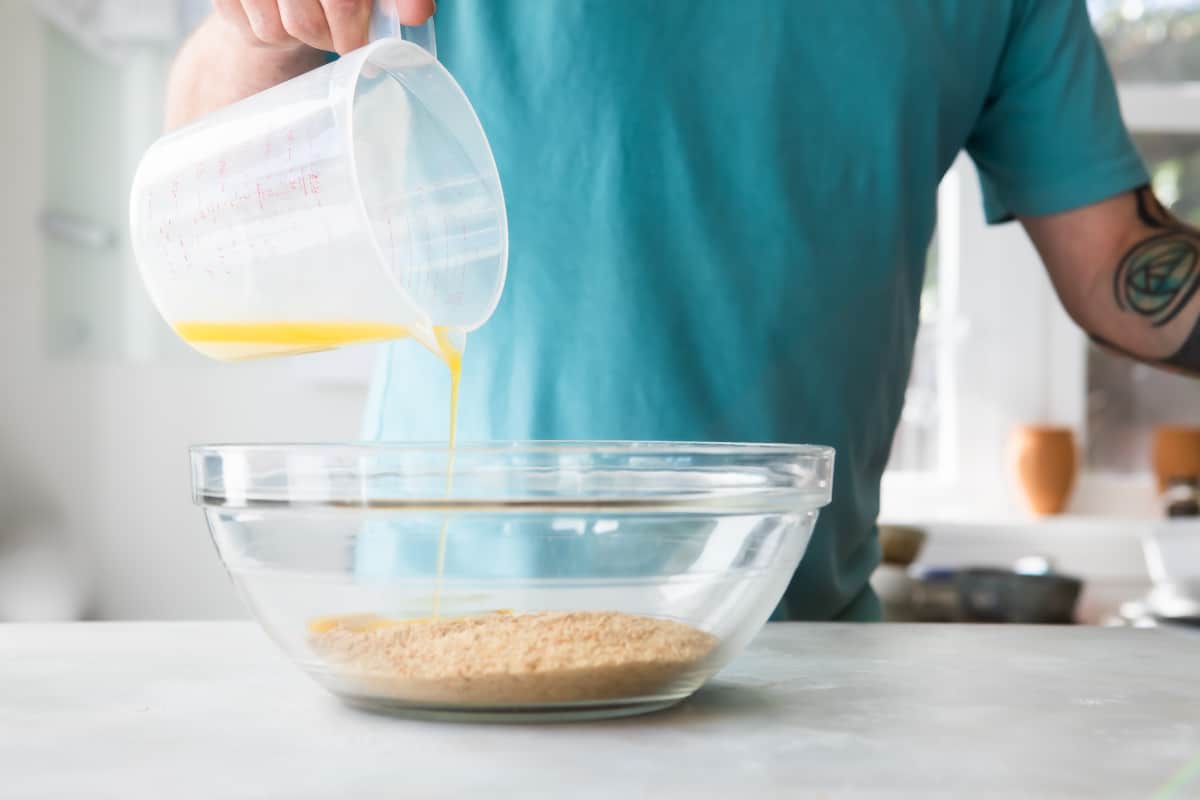 A bowl of graham cracker crumbs with butter being poured in.