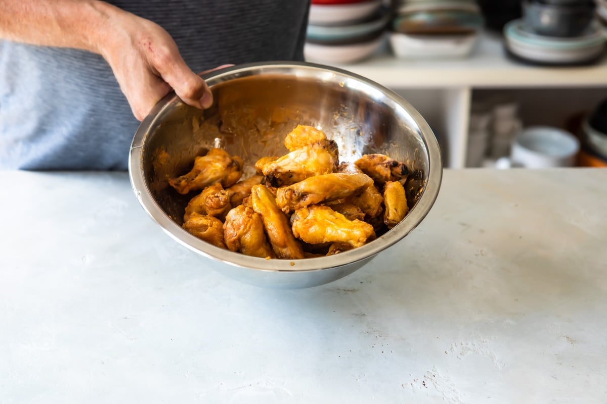 Buffalo wings being tossed in buffalo sauce.