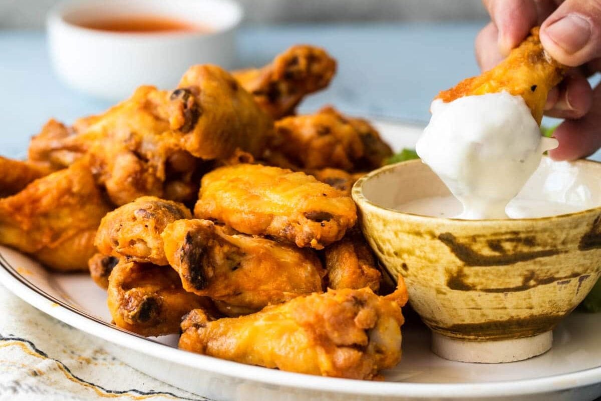 Someone dipping a buffalo chicken wing in blue cheese dressing.