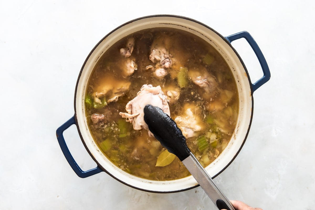Chicken thighs being removed from Booyah stew in a Dutch oven.