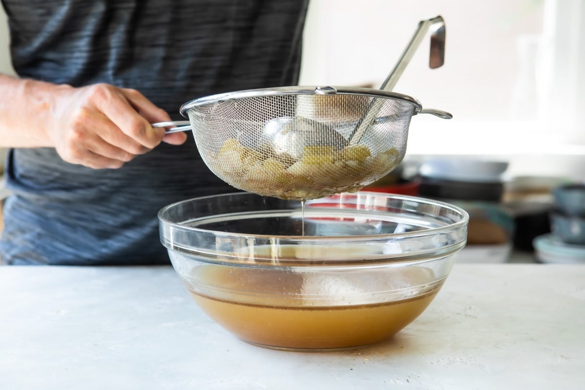 Booyah stew being strained over a clear bowl.