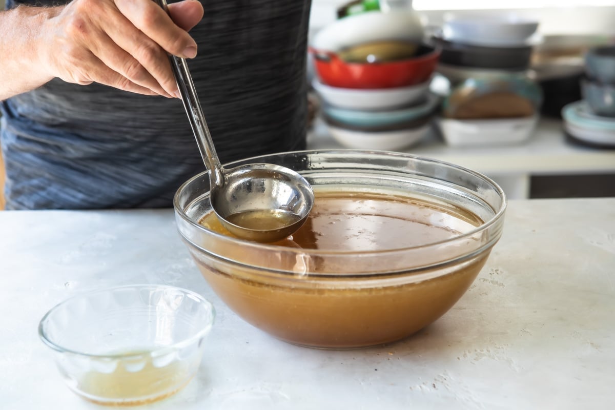 Fat being skimmed off of the top of a brown bowl of liquid.