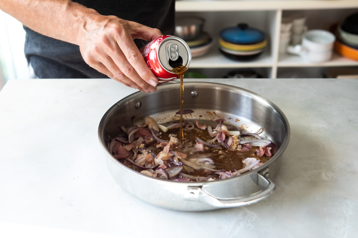 Coca cola being poured into a silver skillet.