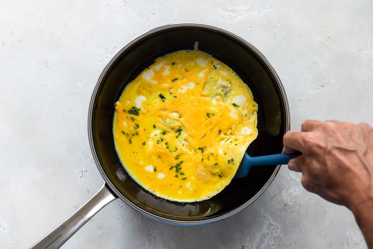 Someone making an egg burrito in a frying pan.