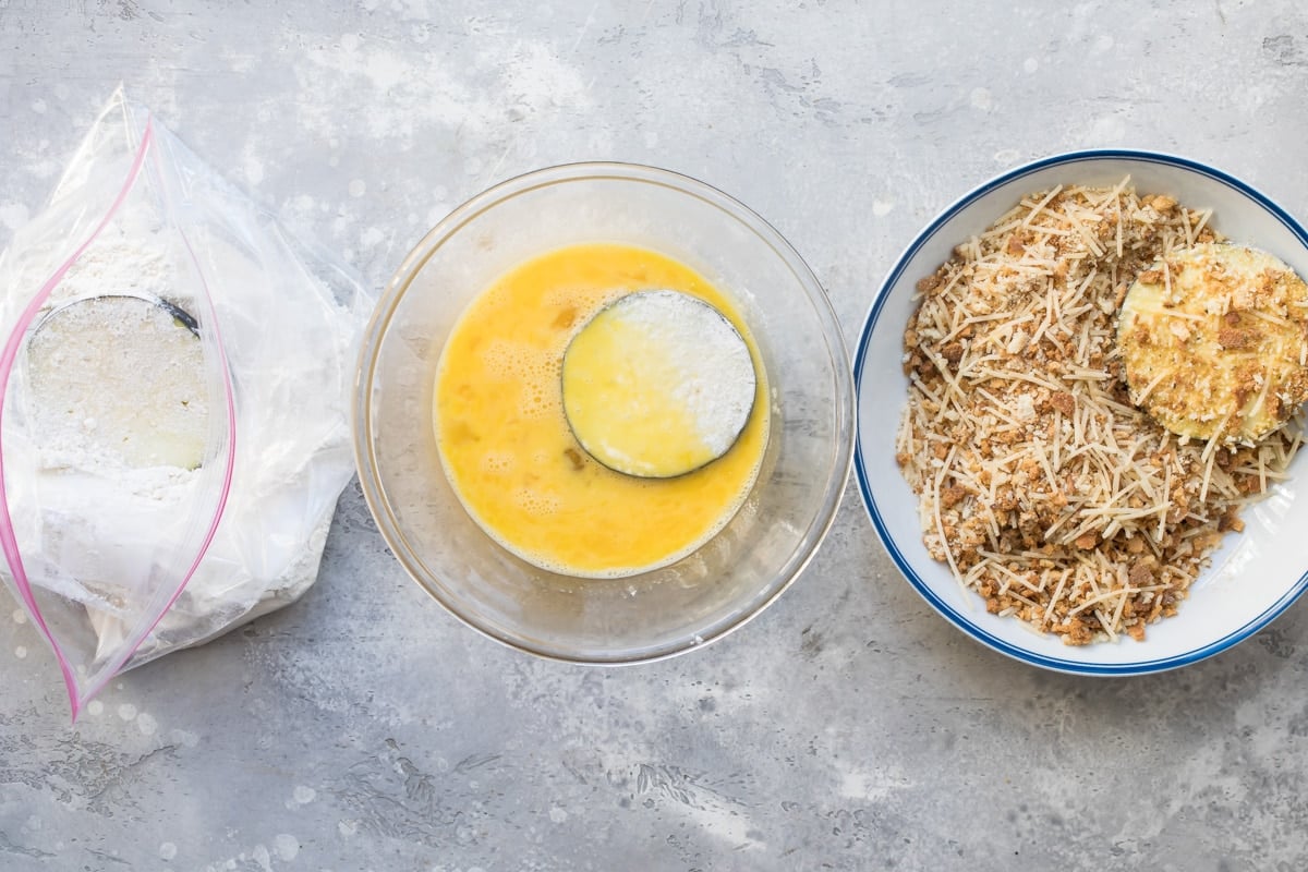 Slices of eggplant being dipped in flour, egg, and shaved parmesan.