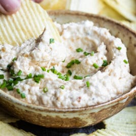 A chip being dipped into French onion dip in a brown bowl.