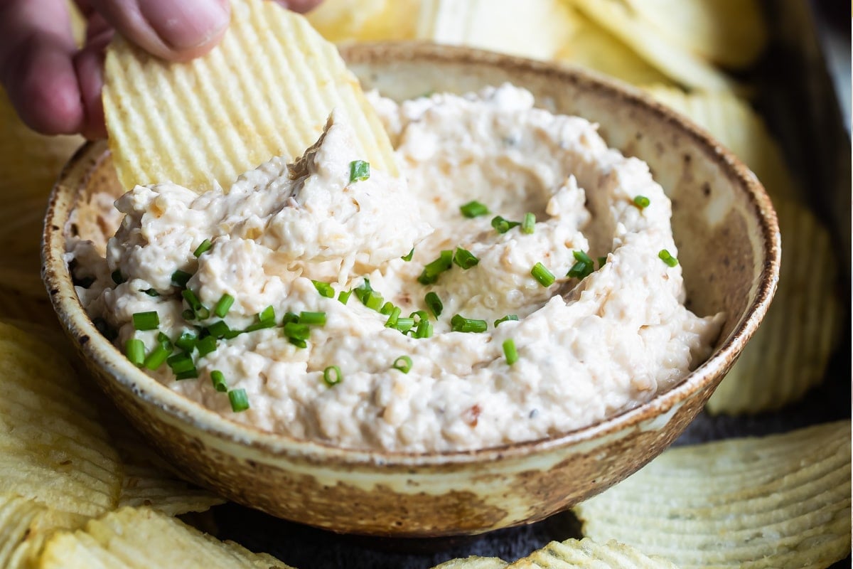 A chip being dipped into French onion dip in a brown bowl.