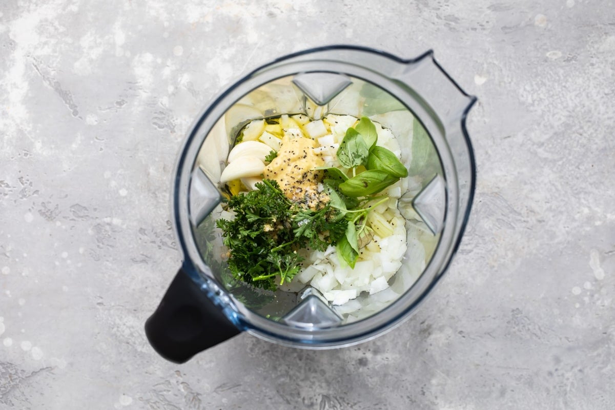 A blender with garlic, herbs, and spices in it to make a marinade for grilled shrimp.