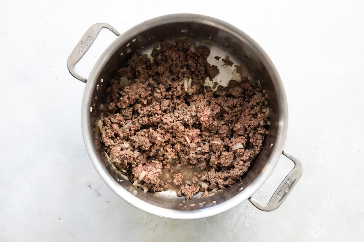 Ground beef and onions in a silver pot.