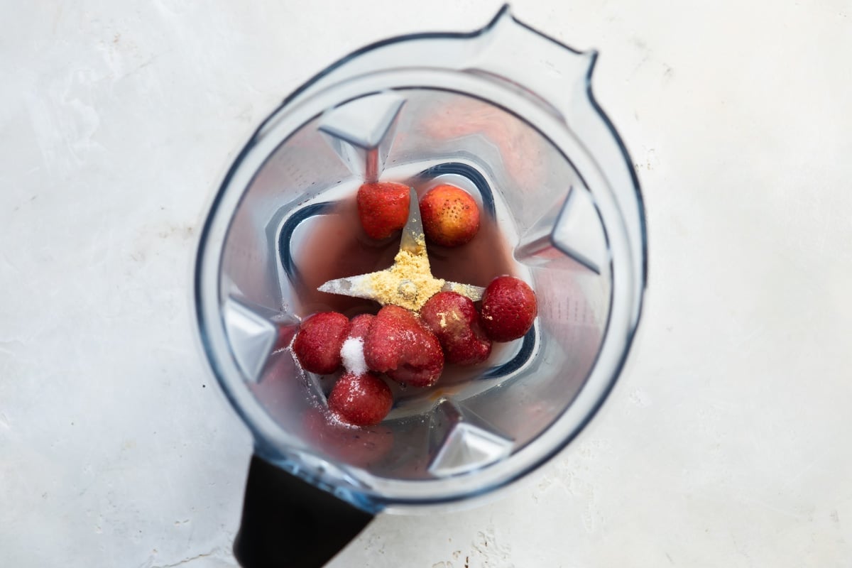 Strawberries and other wet ingredients in a blender before being blended.