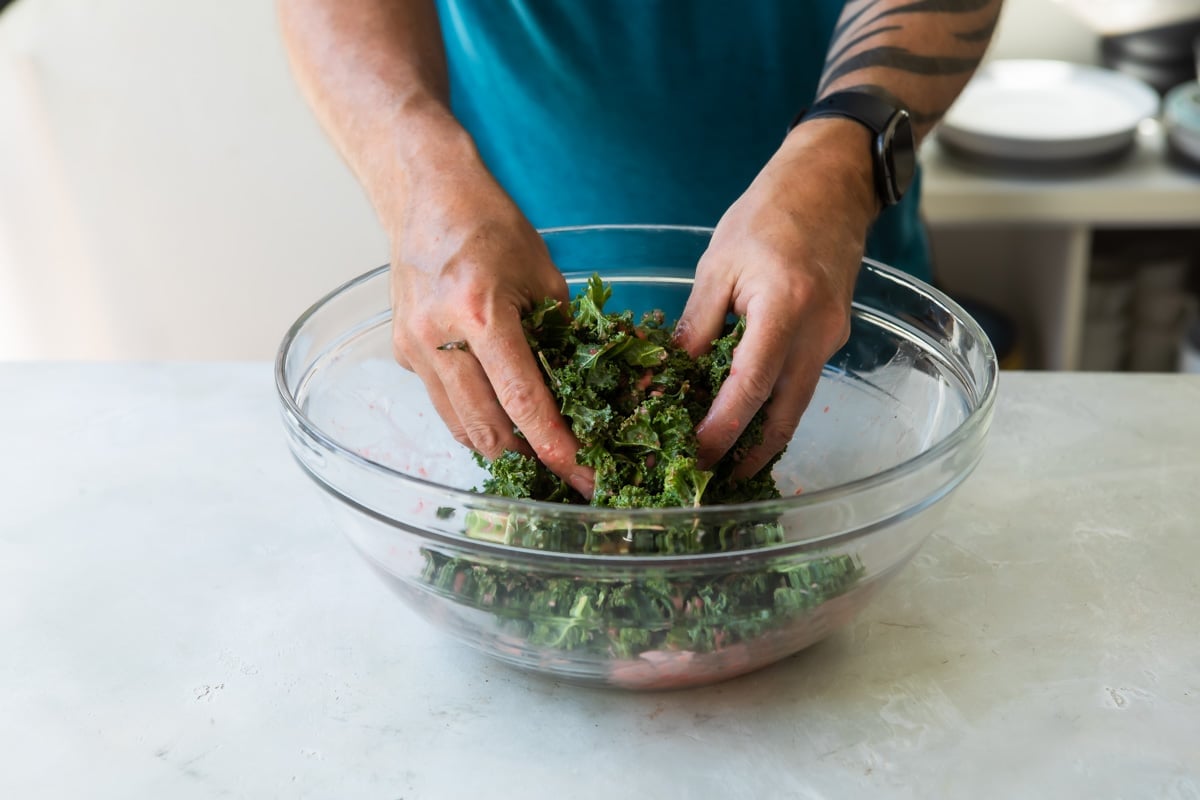 Someone mixing kale salad in a clear bowl.