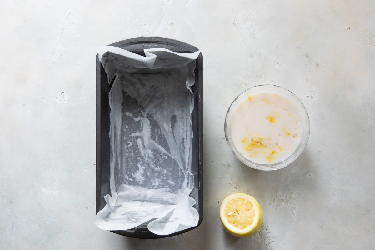 A cake pan next to a bowl with a white mixture and a piece of lemon.