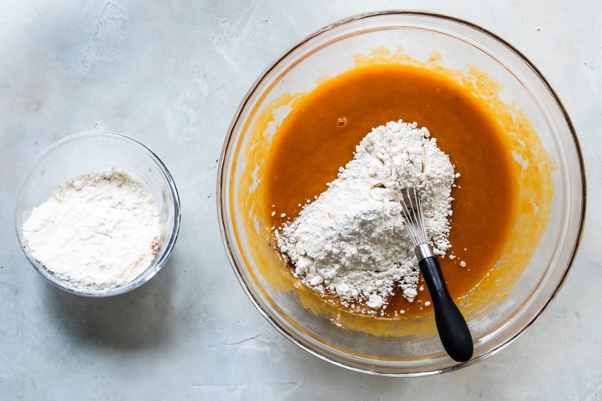 A bowl of pumpkin muffin batter with dry ingredients being whisked in.