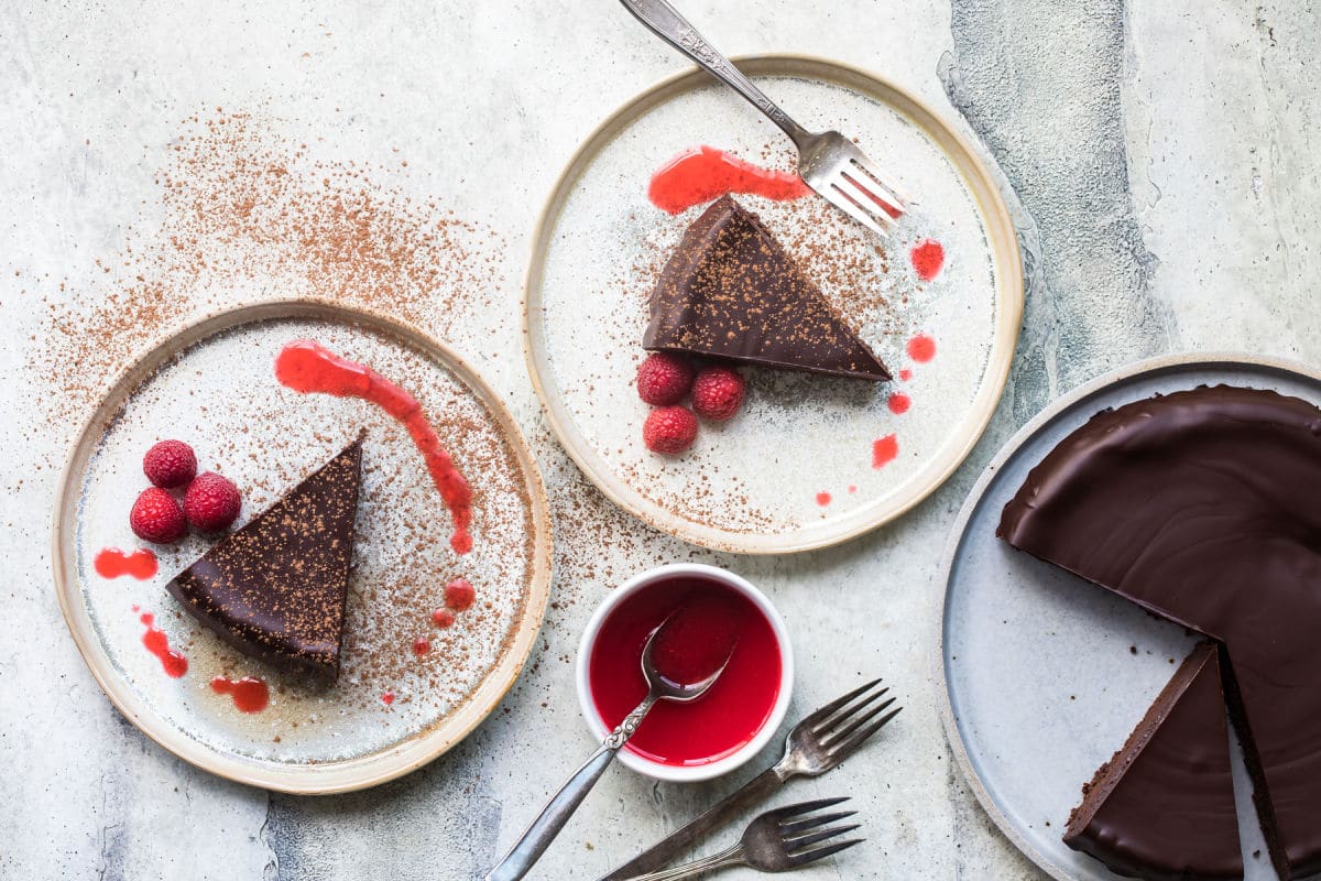 Raspberry coulis in a small white bowl and two white plates with flourless chocolate cake slices.