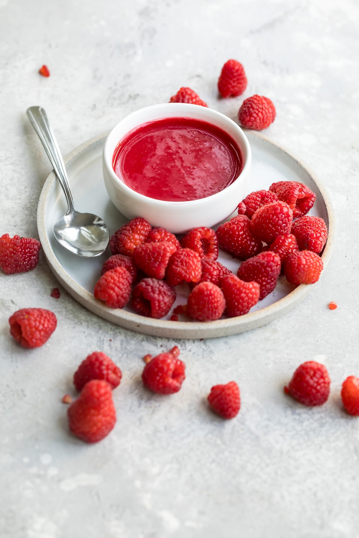 Raspberry coulis in a white dish on a white plate with raspberries.