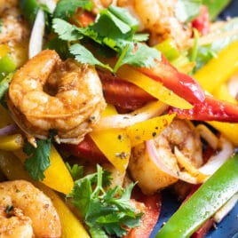 Shrimp fajitas on a blue plate with a side of rice and flour tortillas.