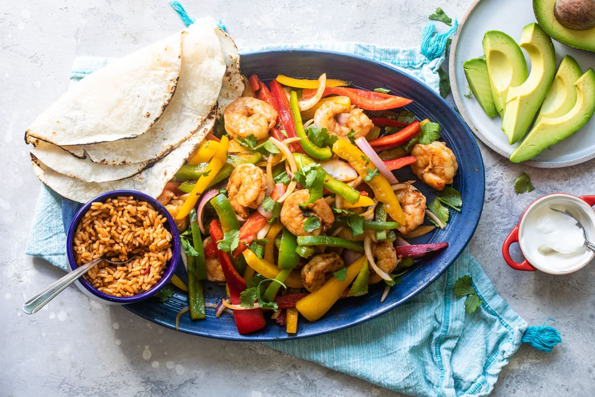 Shrimp fajitas on a blue plate with a side of rice and flour tortillas.
