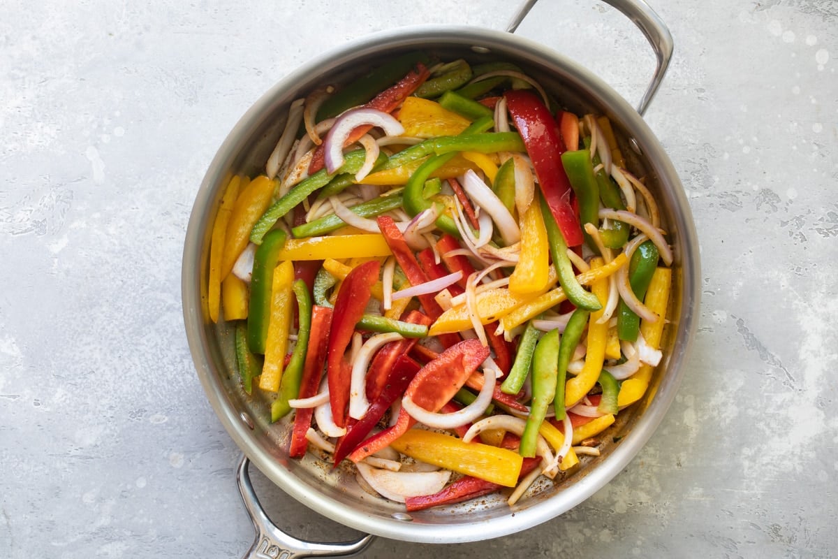 Shrimp fajita veggies sauteing in a sliver pan.